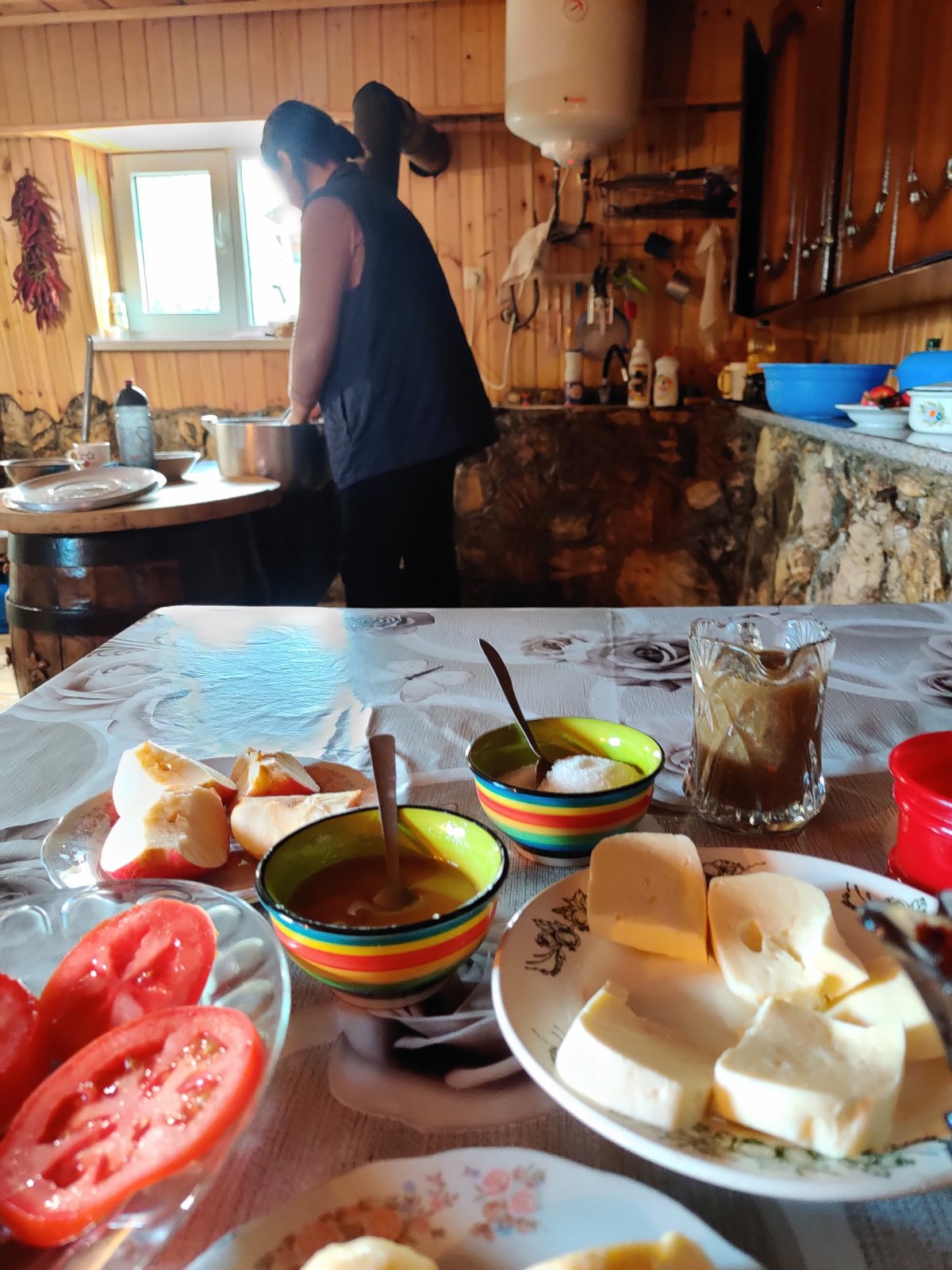 Tradiční domácí snídaně, v pozadí paní domu a dům postavený vlastníma rukama